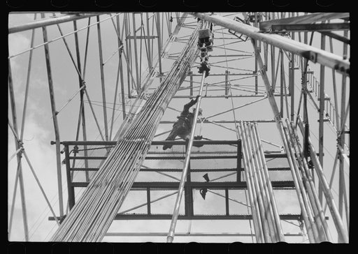 Untitled photo, possibly related to: Looking up in an oil derrick. Roughneck inserting lengths of pipe into the elevator for pulling the casings. Oklahoma City, Oklahoma