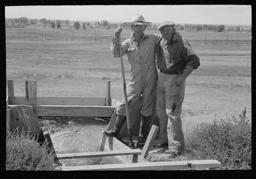 Cooperation in wells for irrigation purposes. Mr. Johnson and Mr. Wright, FSA (Farm Security Administration) clients, standing at the weir box, Syracuse, Kansas