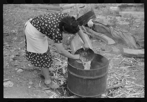 Spanish-American FSA (Farm Security Administration) client emptying pail of grease into kettle for purpose of making soap, Taos County, New Mexico
