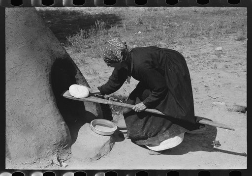 Spanish-American woman putting loaf of bread into oven, Taos County, New Mexico