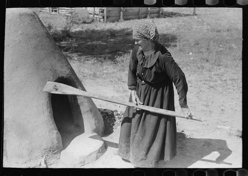 Spanish-American woman testing temperature of earthen oven by determining length of time required to scorch wool, Taos County, New Mexico