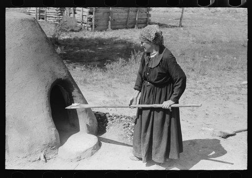 Spanish-American woman testing temperature of earthen oven by determining length of time required to scorch wool, Taos County, New Mexico