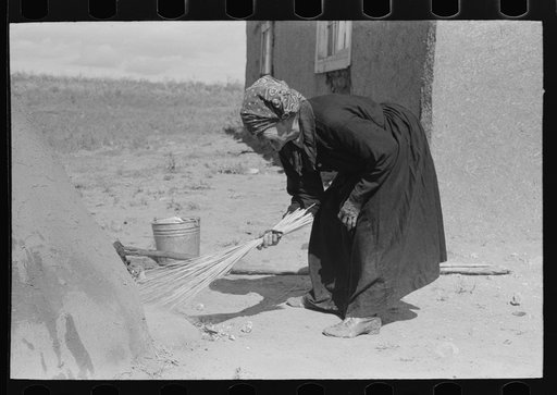 Sweeping hot coals from outdoor earthen oven after it has been heated to proper temperature to bake bread, Taos County, New Mexico