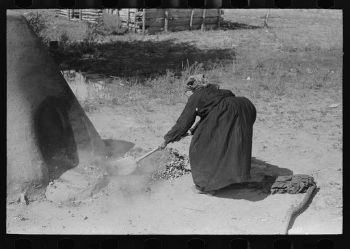 Sweeping coals and ashes from oven before baking bread, Taos County, New Mexico