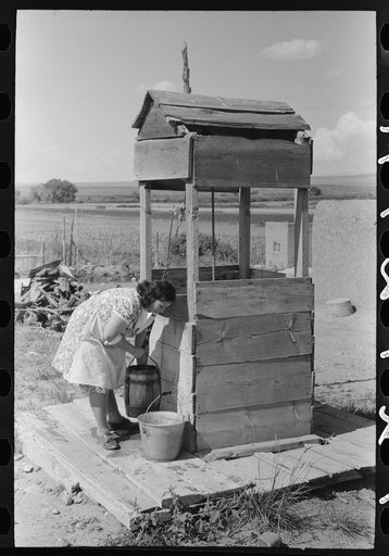 Daughter of Spanish-American farm family drawing water at the well, Taos County, New Mexico