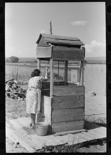 Daughter of Spanish-American farm family drawing water at the well, Taos County, New Mexico