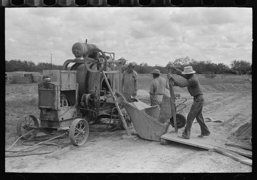 Dumping materials into concrete mixer at migrant camp under construction at Sinton, Texas