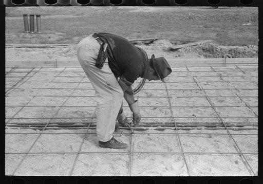 Tying iron reinforcement bars together before pouring concrete at migrant camp under construction at Sinton, Texas