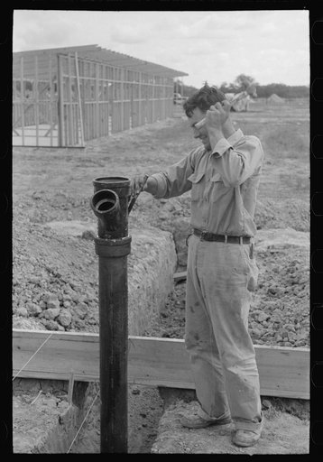 Working on sewer pipe connection at migrant camp under construction at Sinton, Texas