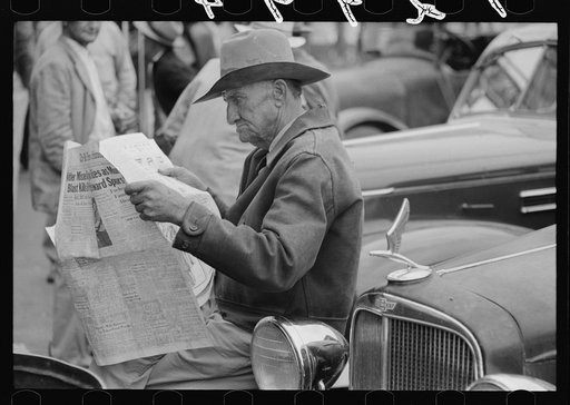 Man sitting on automobile fender reading a newspaper, market square, Waco, Texas