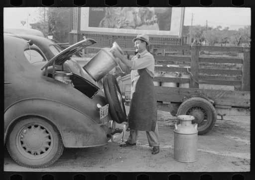 Loading empty milk cans into back of car, creamery, San Angelo, Texas