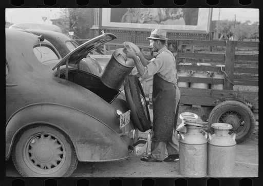 Loading empty milk cans into back of car, creamery, San Angelo, Texas