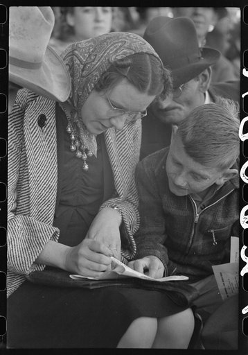 Spectators at the rodeo looking at the program. San Angelo Fat Stock Show, San Angelo, Texas