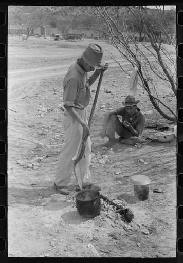 Professional goat and sheep shearer moving kettle closer to the coals while he cooks the noonday mean on the ranch of a rehabilitation borrower in Kimble County, Texas