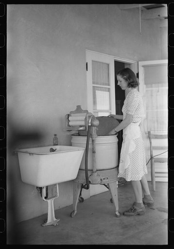 Woman living at the Casa Grande Valley Farms, Pinal County, Arizona, removing the cover from her electric washing machine