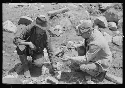 Gold prospector on the right who is working a claim down the canyon is visiting and examining ore speciman of the prospector on left. Pinos Altos, New Mexico