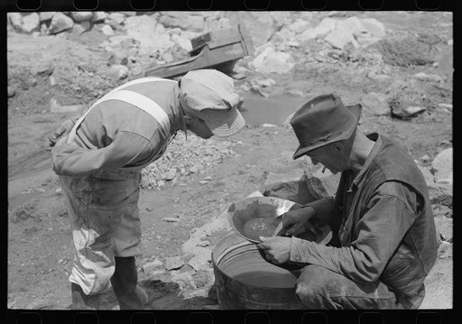 Miner on right examining a "pan" while the visiting prospector watches. Pinos Altos, New Mexico