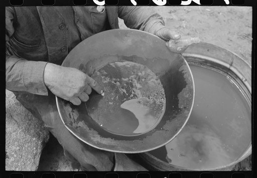 Untitled photo, possibly related to: "Pan" of gold. Not all of the shiny particles are gold but include mica and a few particles of quicksilver. The gold usually appears in the pan as a minute shiny upper rim of the dirt in the pan. Pinos Altos, New Mexico