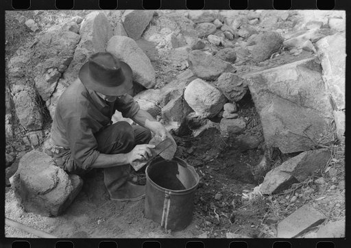 Prospector taking a sample of dirt from a creek bed. There is gold along this creek bed and he is trying, by taking samples all along, to determine its source. Pinos Altos, New Mexico