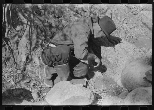 Prospector examining rock formation along creek bed which contains gold. Pinos Altos, New Mexico