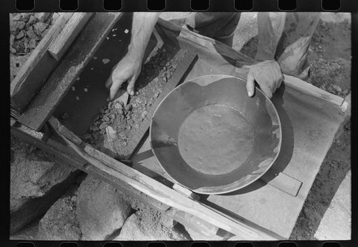 Prospector taking material left in rocker which he will place in pan for the recovery of the gold which it contains. Pinos Altos, New Mexico