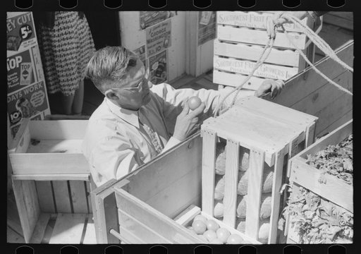 Mr. Keele examining oranges before buying them from trucker. General store. Pie Town, New Mexico