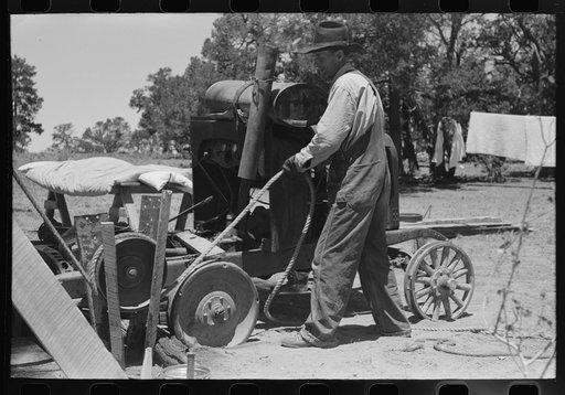 Farmer drilling water well. In this picture he is loosening and tightening rope around the pulley, thus raising and lowering the drilling tool. Pie Town, New Mexico