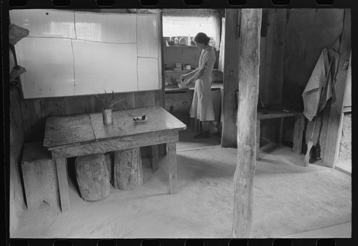 Mrs. Whinery working in her kitchen. This picture shows the dirt floor of the dugout and the natural lighting. Pie Town, New Mexico