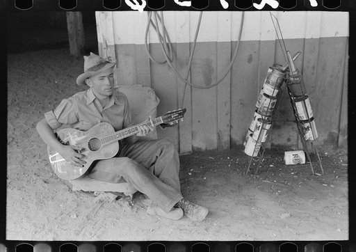 Untitled photo, possibly related to: Farm boy playing guitar in front of the filling station and garage, Pie Town, New Mexico