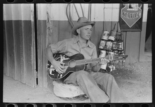 Untitled photo, possibly related to: Farm boy playing guitar in front of the filling station and garage, Pie Town, New Mexico