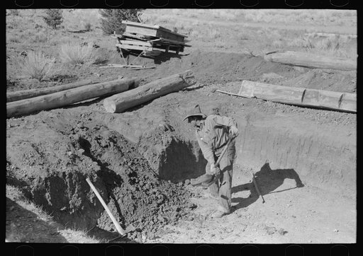 Faro Caudill shoveling out dirt while building steps of his dugout, Pie Town, New Mexico