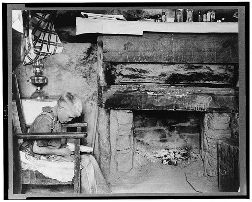 Mr. Leatherman's son reading in front of fireplace in dugout, Pie Town, New Mexico