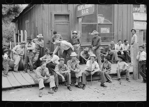 Crowd of men sitting on board walk in front of bar at Mogollon, New Mexico, gold mining town