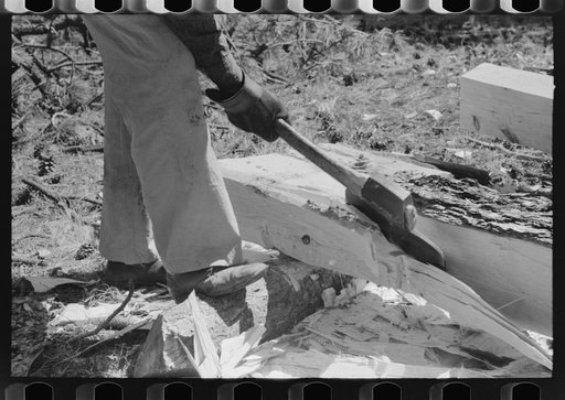 Using a broad axe to remove large chunks from log which will be made into a tie, Pie Town, New Mexico