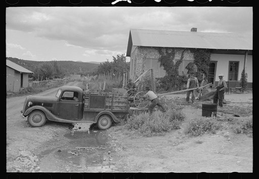 Spanish-American farmers loading a mower onto a track, Chamisal, New Mexico