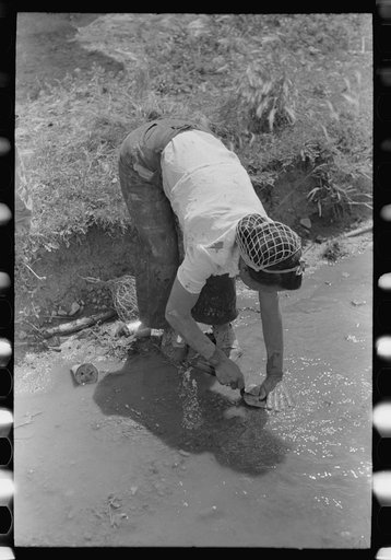 Washing off the plastering trowel in the irrigation ditch, Chamisal, New Mexico