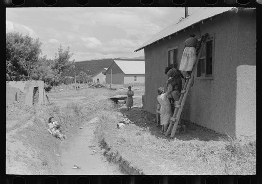 Plastering adobe house and washing near irrigation ditch, Chamisal, New Mexico