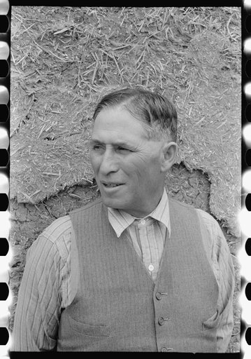 Spanish-American farmer standing in front of adobe wall, Chamisal, New Mexico