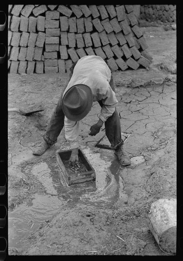 Washing out wooden form and saturating it with water, the first step in making adobe bricks, Chamisal, New Mexico