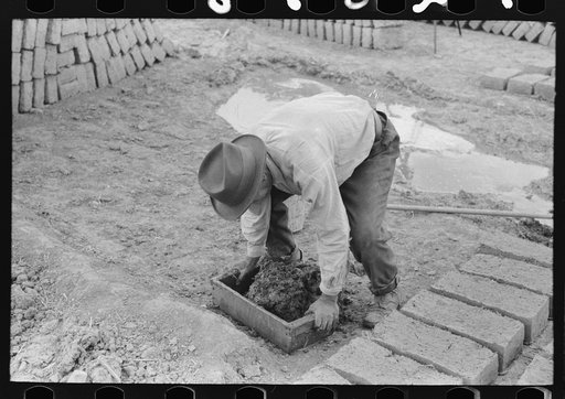 Wooden form is placed over adobe mixture in making bricks, Chamisal, New Mexico