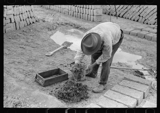 Adding water to adobe mixture for making bricks, Chamisal, New Mexico
