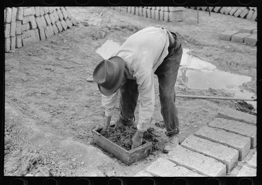 Kneading adobe in wooden form for making bricks. Chamisal, New Mexico