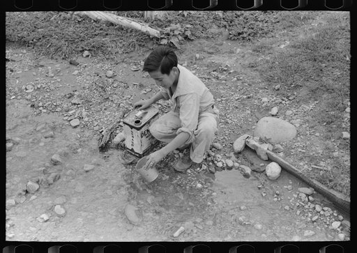 Untitled photo, possibly related to: A Spanish-American boy dipping water from irrigating ditch. Water will be used in house for cooking, drinking, etc. Chamisal, New Mexico