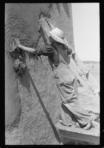 Spanish-American woman plastering adobe house, Chamisal, New Mexico