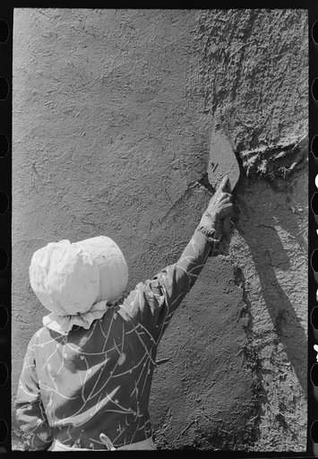 Spanish-American woman plastering adobe house, Chamisal, New Mexico