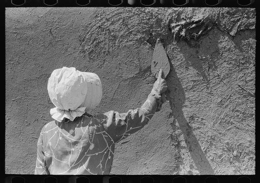 Spanish-American woman plastering adobe house, Chamisal, New Mexico