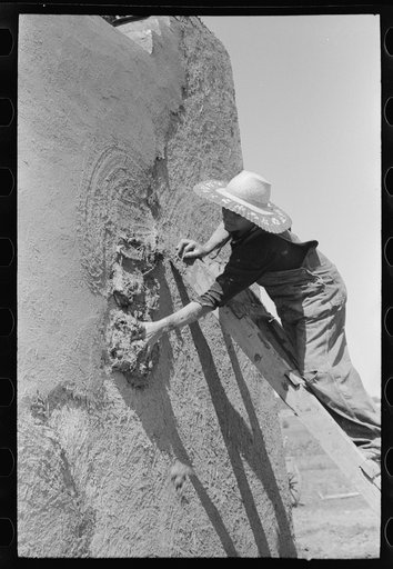 Spanish-American woman plastering adobe house, Chamisal, New Mexico