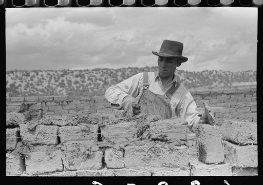 Putting adobe plaster between adobe bricks in construction of house, Penasco, New Mexico