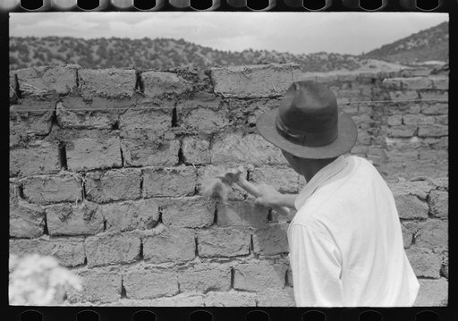 Shaping up wall made of adobe bricks to remove rough or uneven edges, Penasco, New Mexico