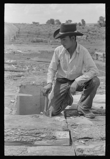 Spanish-American boy on top of house. He is building a new roof. Amalia, New Mexico